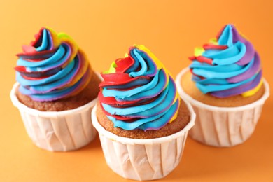 Delicious cupcakes with colorful cream on orange background, closeup