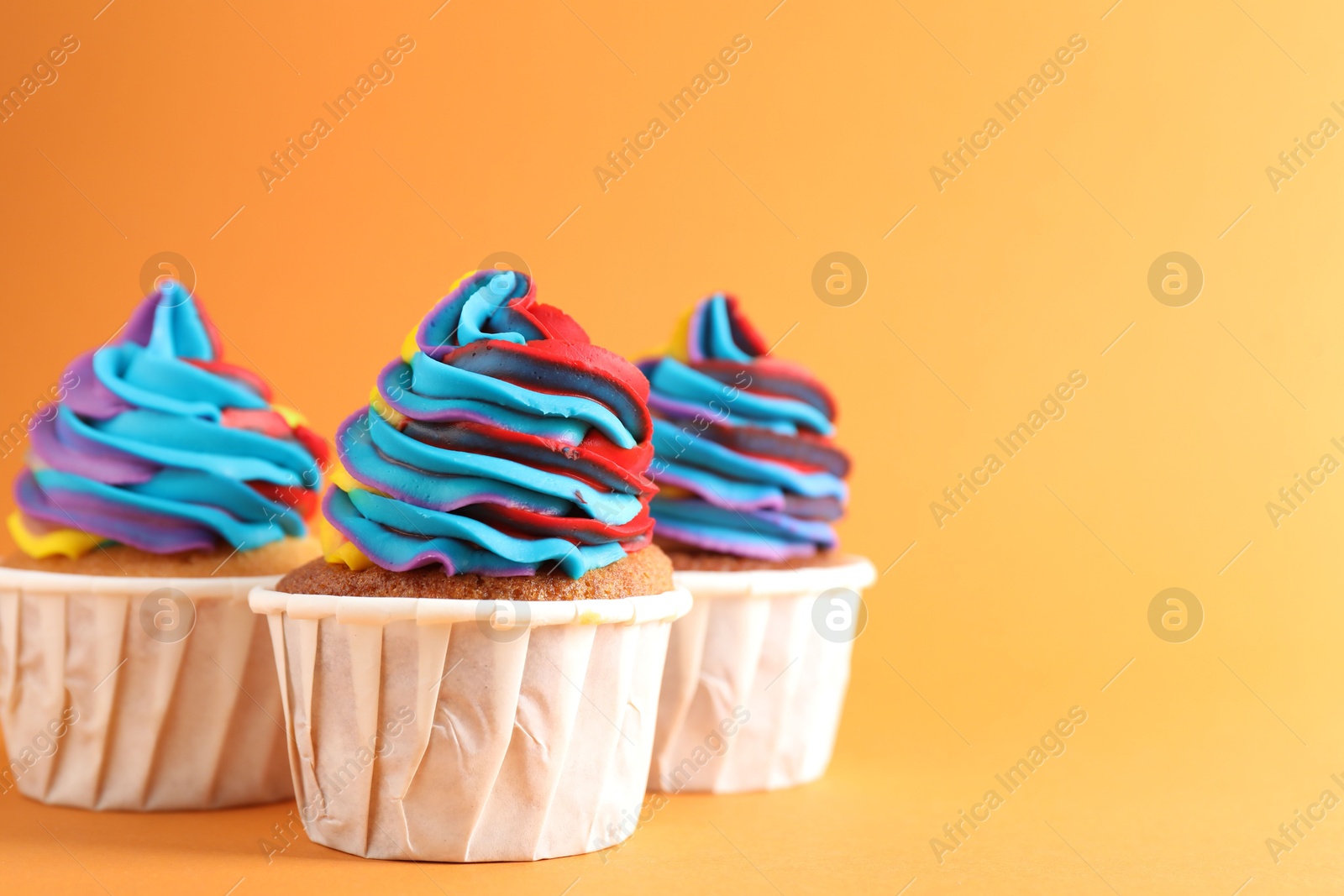 Photo of Delicious cupcakes with colorful cream on orange background, closeup. Space for text