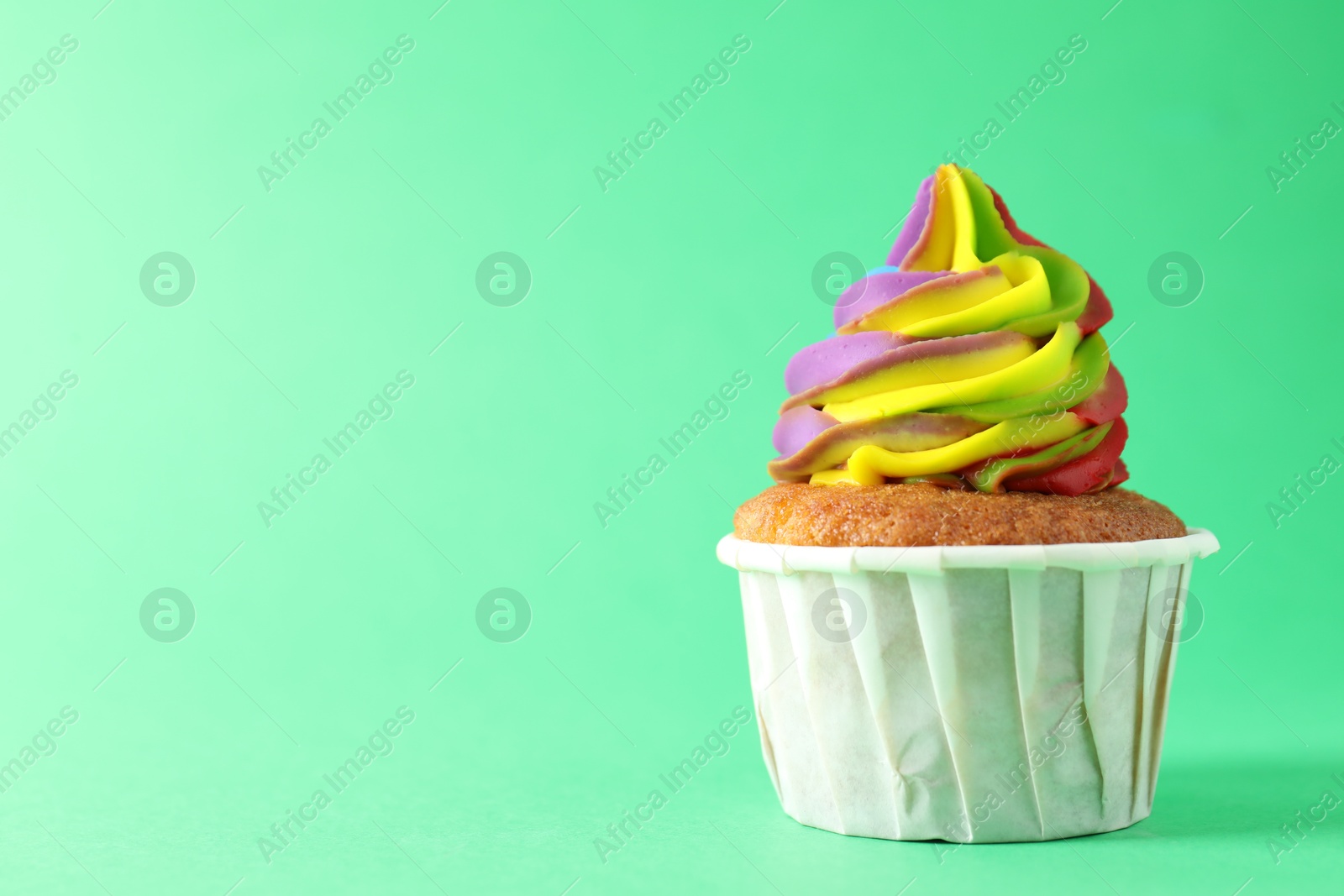 Photo of One delicious cupcake with colorful cream on green background, closeup. Space for text