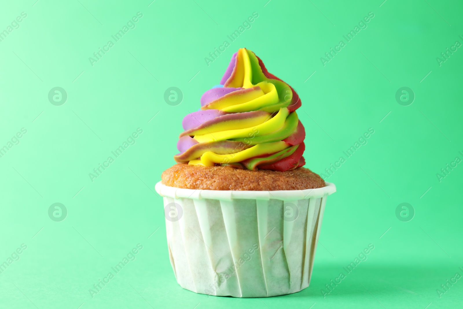 Photo of One delicious cupcake with colorful cream on green background, closeup