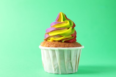 Photo of One delicious cupcake with colorful cream on green background, closeup