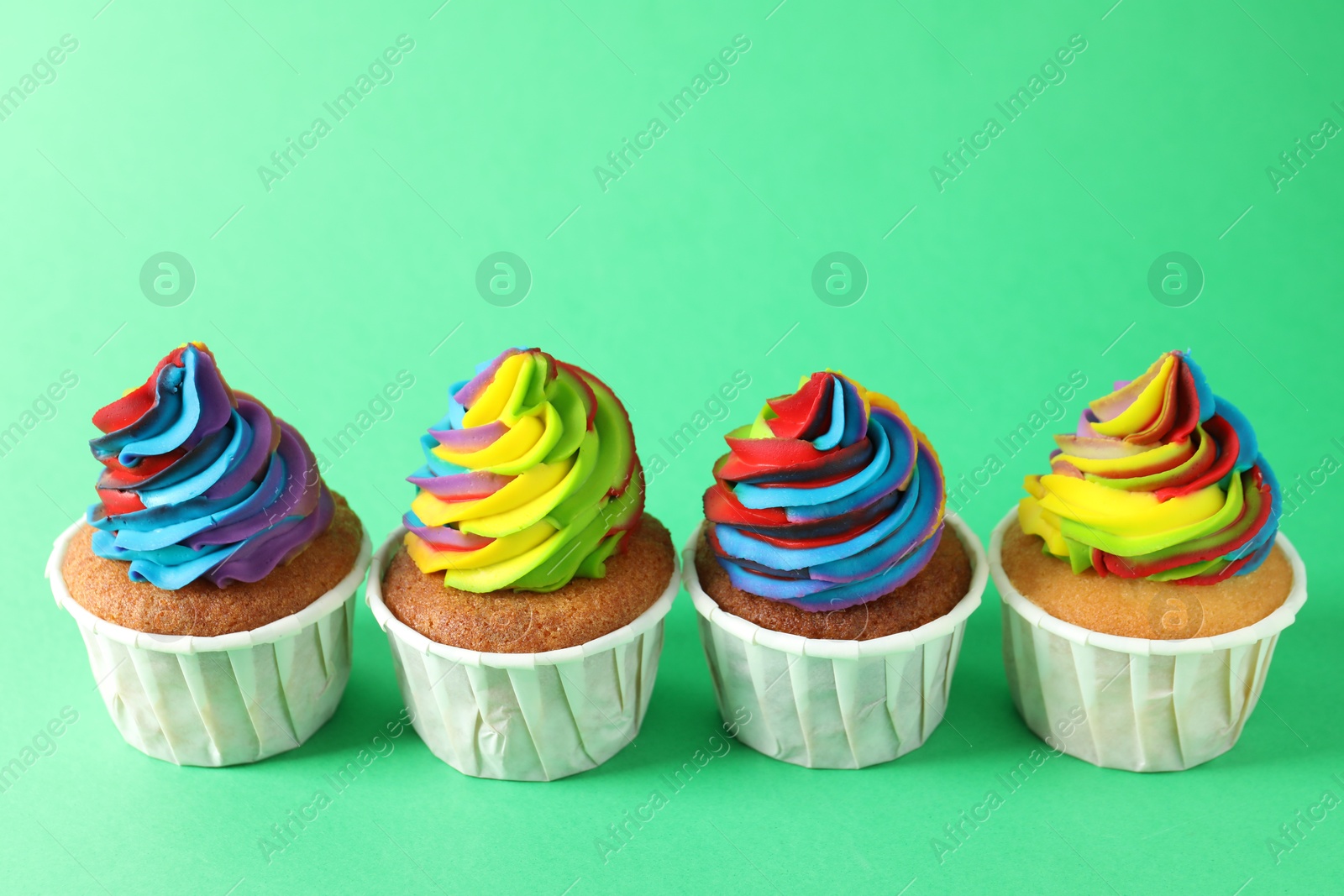 Photo of Delicious cupcakes with colorful cream on green background, closeup