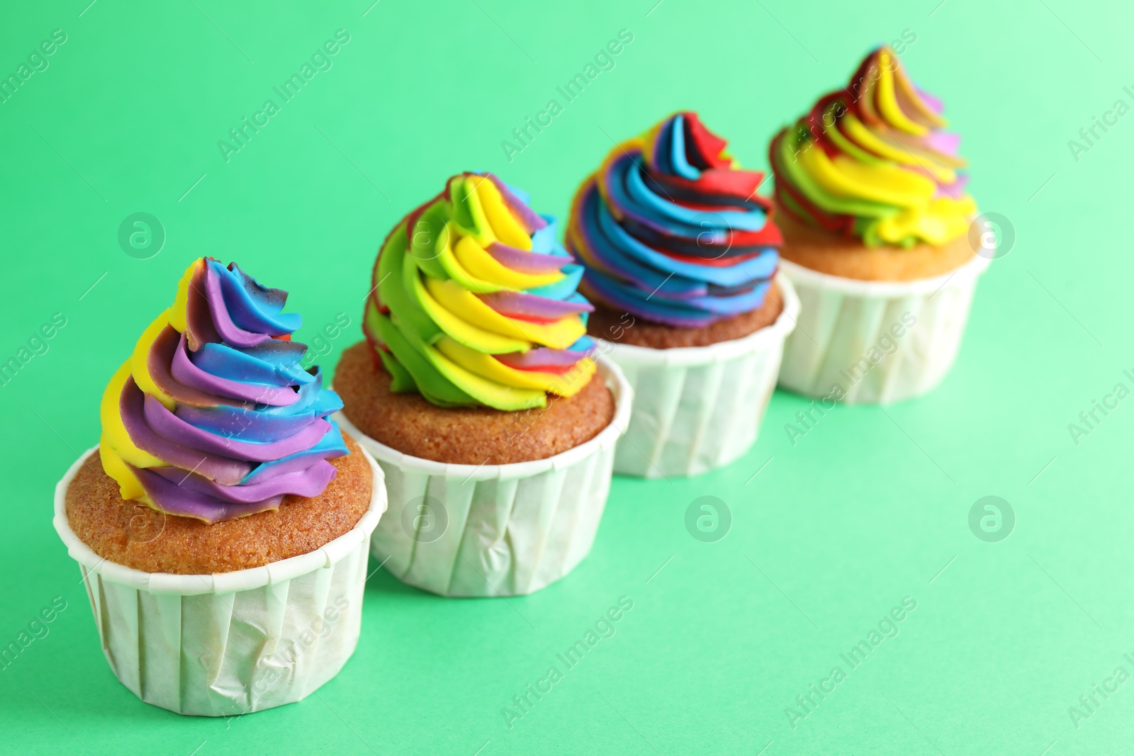 Photo of Delicious cupcakes with colorful cream on green background, closeup