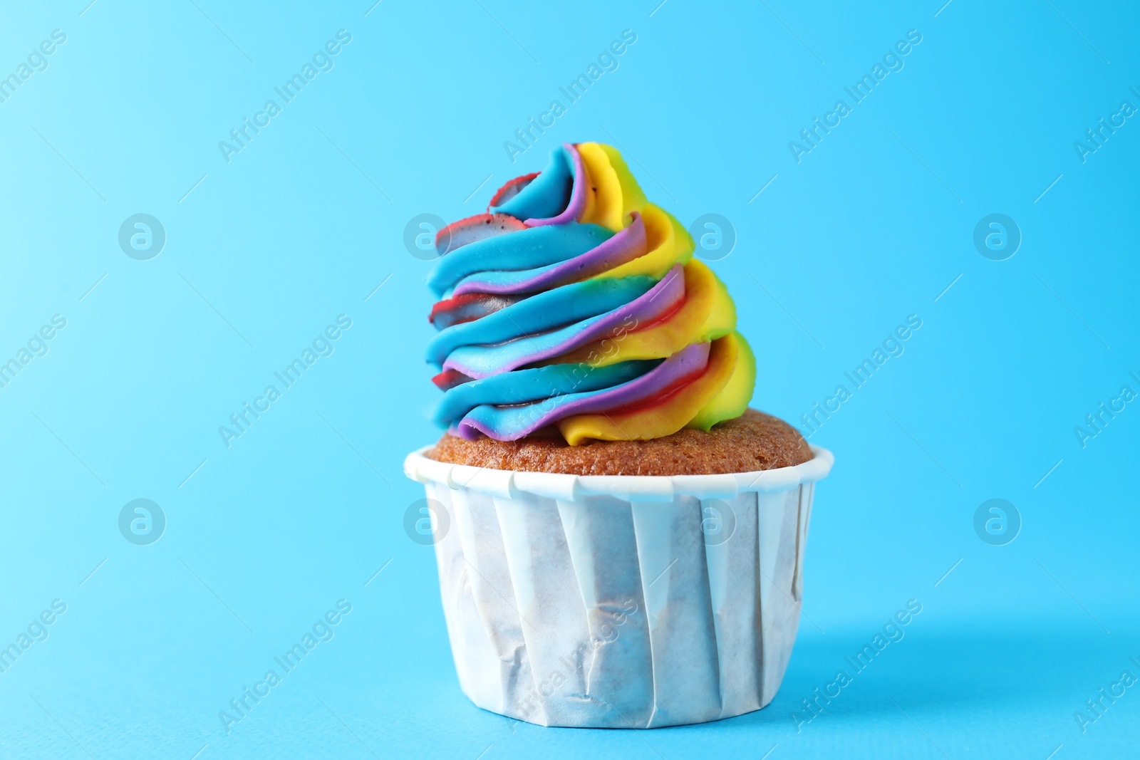 Photo of One delicious cupcake with colorful cream on light blue background, closeup