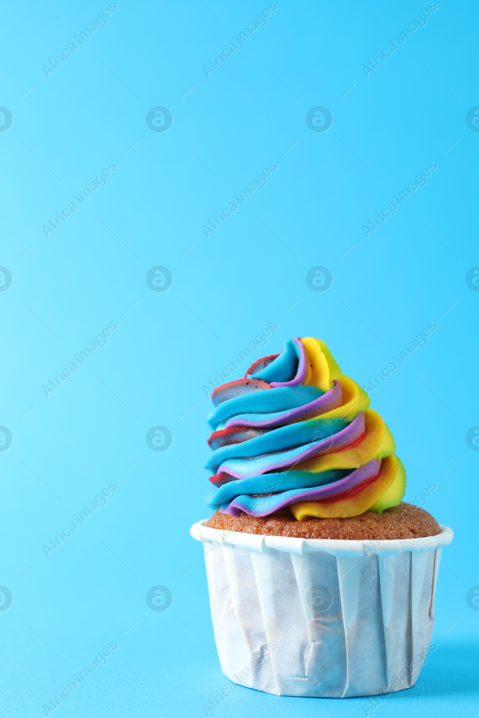 Photo of One delicious cupcake with colorful cream on light blue background, closeup. Space for text