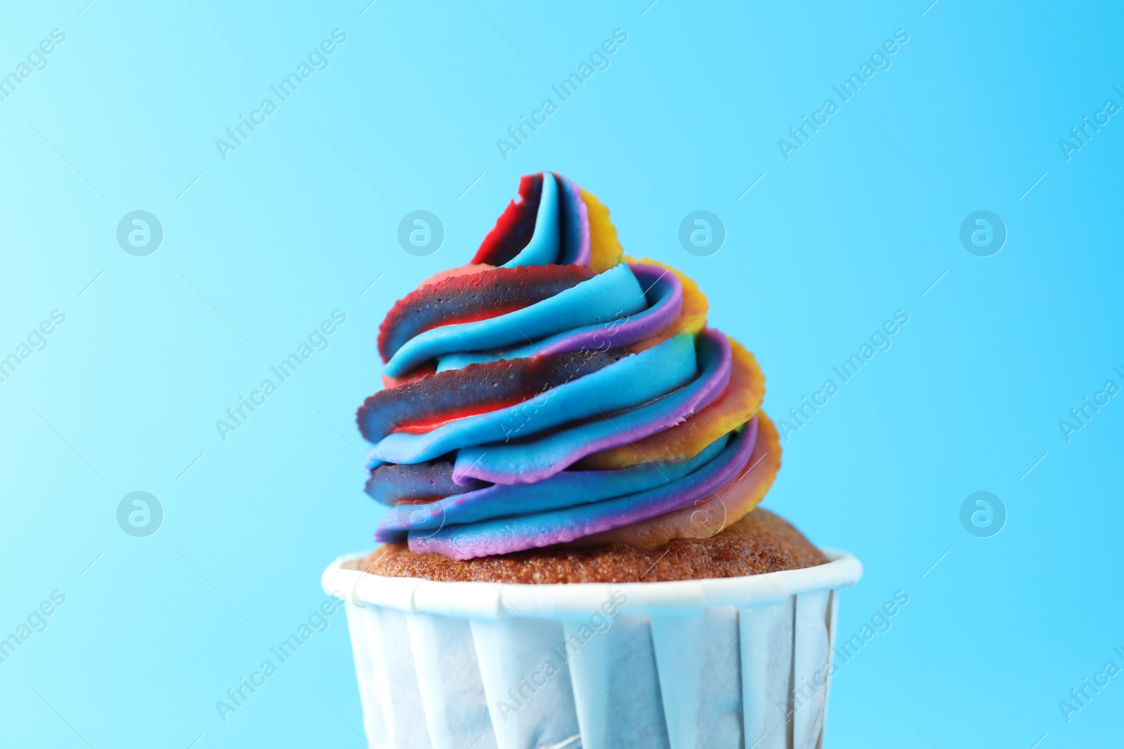 Photo of One delicious cupcake with colorful cream on light blue background, closeup