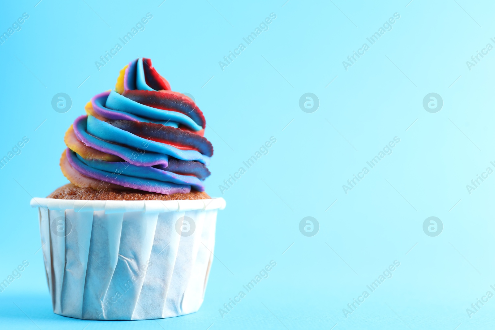 Photo of One delicious cupcake with colorful cream on light blue background, closeup. Space for text