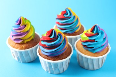 Photo of Delicious cupcakes with colorful cream on light blue background, closeup