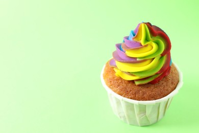 Photo of One delicious cupcake with colorful cream on light green background, closeup. Space for text