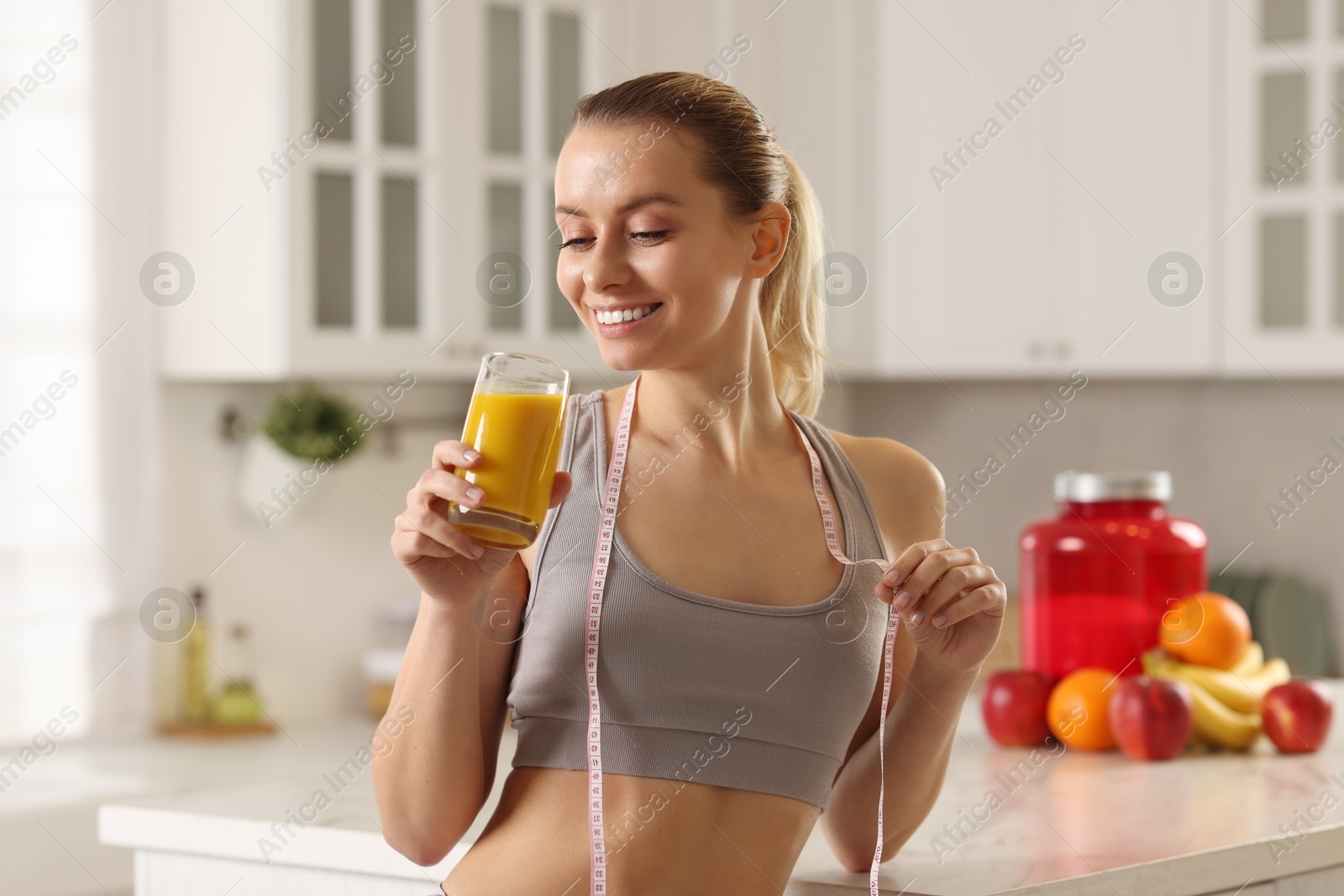 Photo of Weight loss. Happy woman with tasty shake and measuring tape in kitchen