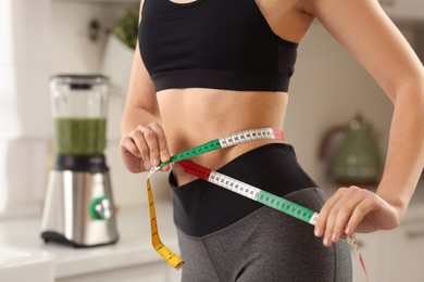 Photo of Weight loss. Woman measuring waist with tape in kitchen, closeup