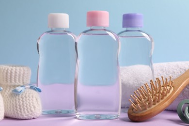 Photo of Baby oil in bottles, pacifier, brush and accessories on violet table against light blue background, closeup