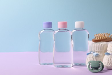 Photo of Baby oil in bottles, pacifier, brush and accessories on violet table against light blue background. Space for text