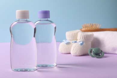 Photo of Baby oil in bottles, pacifier, brush and accessories on violet table against light blue background, closeup