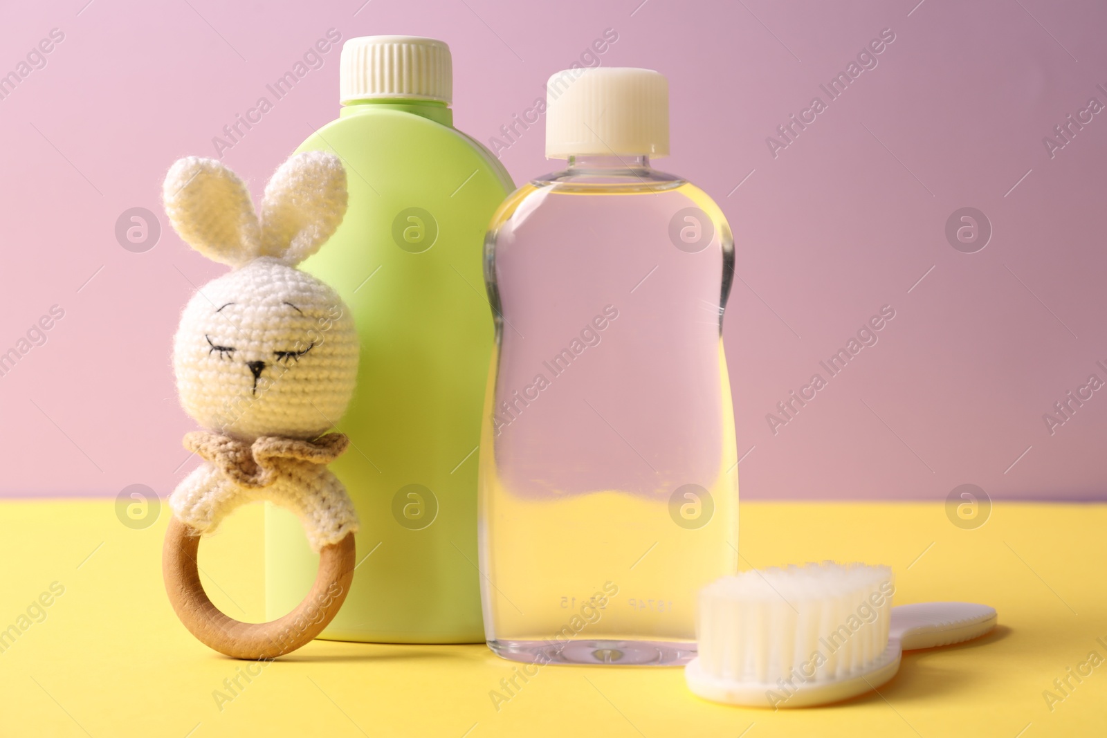 Photo of Baby care products, rattle and brush on yellow table against violet background, closeup