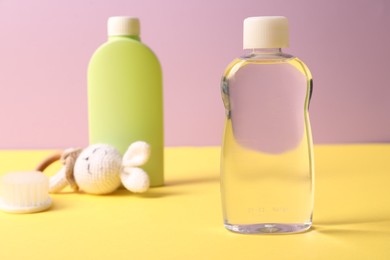 Photo of Baby care products, rattle and brush on yellow table against violet background, selective focus