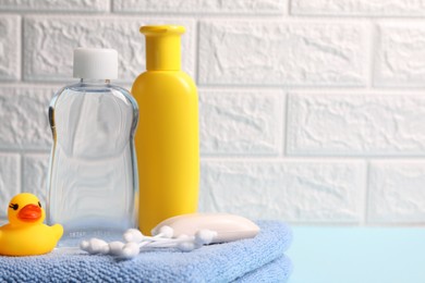 Photo of Baby care products and bath accessories on light blue table against white brick wall, closeup. Space for text