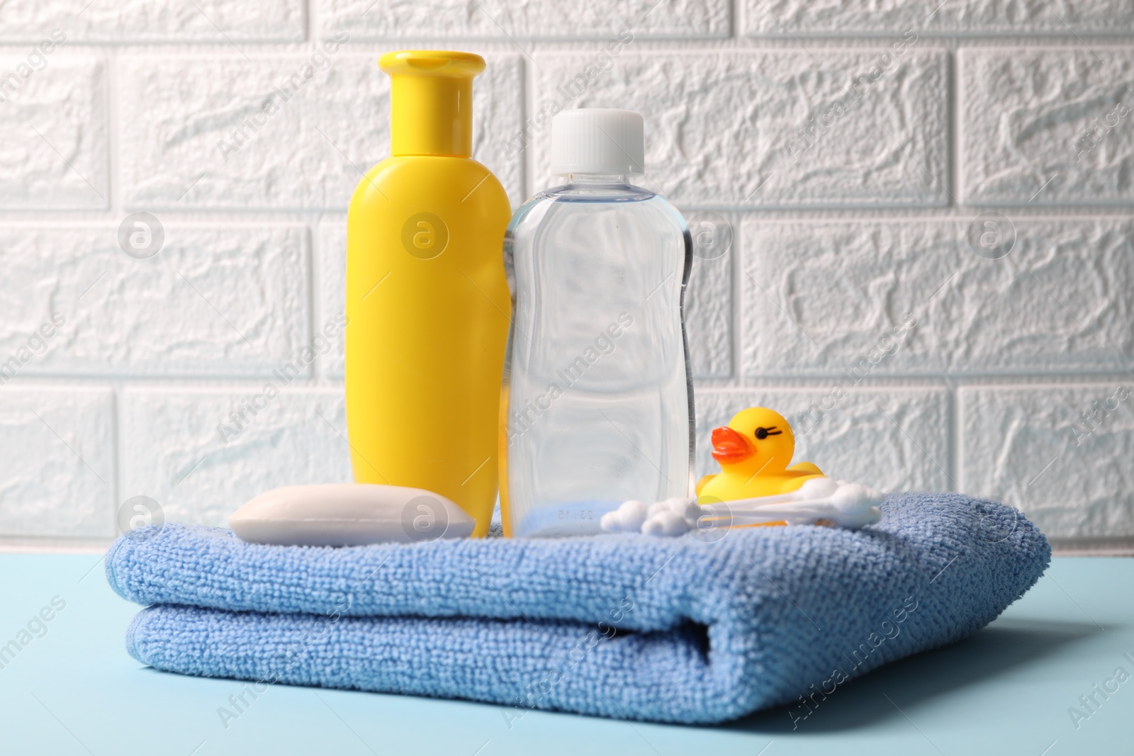 Photo of Baby care products and bath accessories on light blue table against white brick wall, closeup