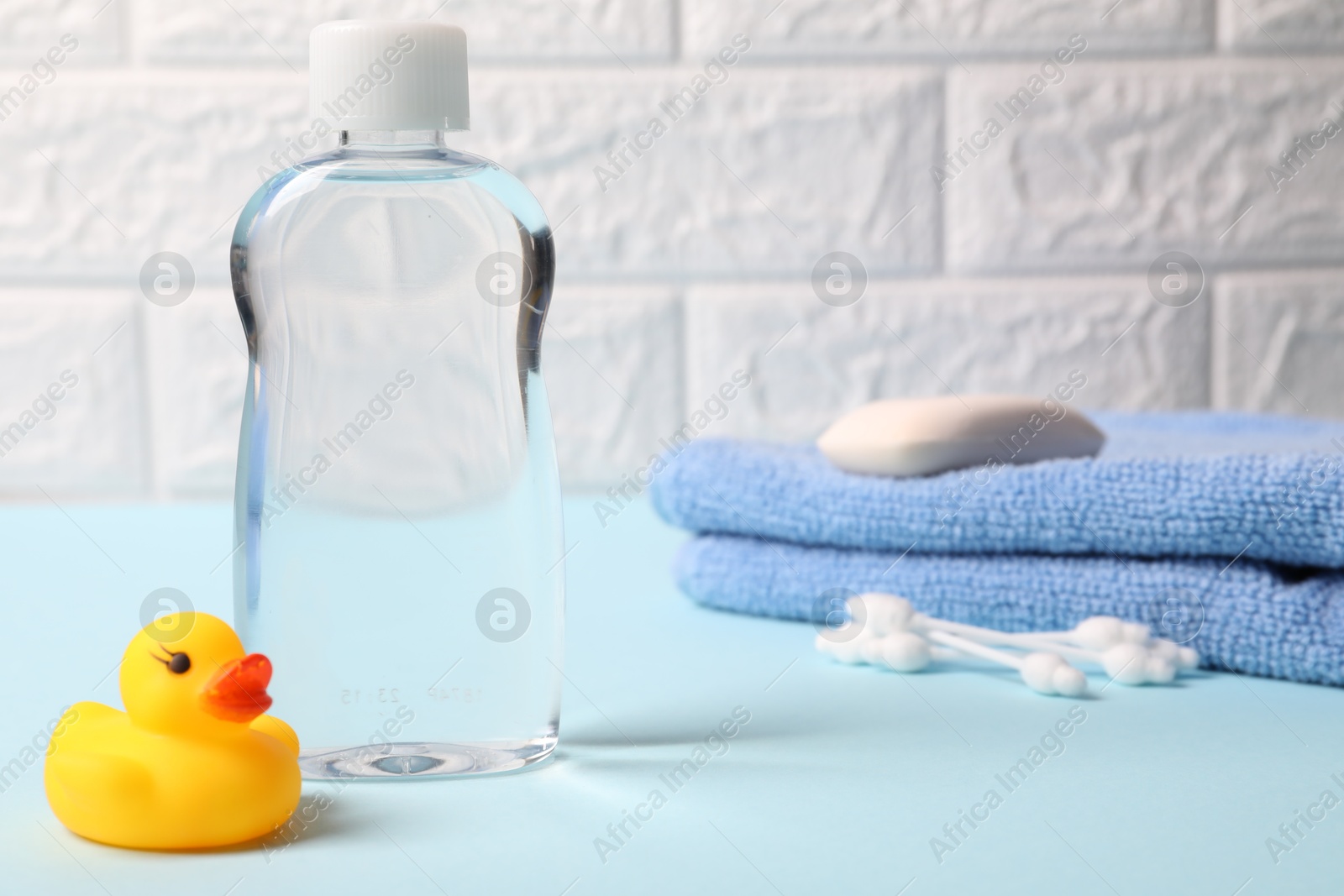 Photo of Baby care products and bath accessories on light blue table against white brick wall, selective focus