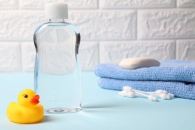 Photo of Baby care products and bath accessories on light blue table against white brick wall, selective focus