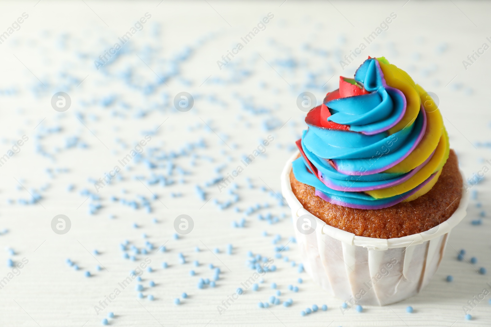 Photo of One delicious cupcake with colorful cream and sprinkles on white wooden table, closeup. Space for text