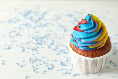 Photo of One delicious cupcake with colorful cream and sprinkles on white wooden table, closeup. Space for text