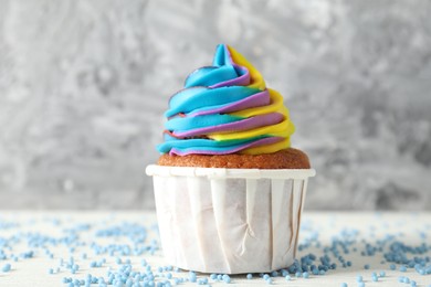 Photo of One delicious cupcake with colorful cream and sprinkles on white wooden table against blurred grey background, closeup