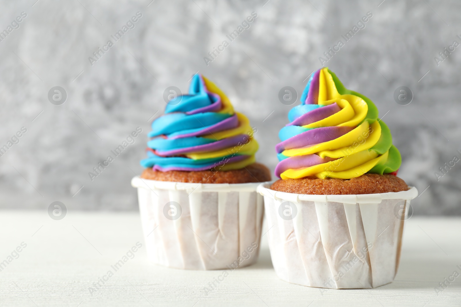 Photo of Delicious cupcakes with colorful cream on white wooden table against blurred grey background, closeup. Space for text