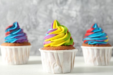 Photo of Delicious cupcakes with colorful cream on white wooden table against blurred grey background, closeup