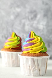 Photo of Delicious cupcakes with colorful cream on white wooden table against blurred grey background, closeup