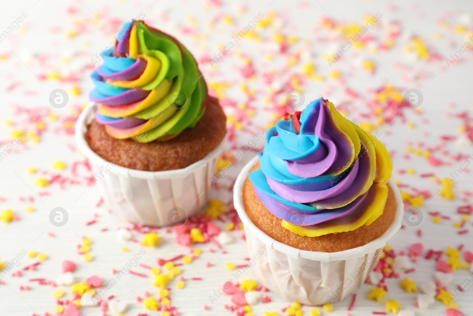 Photo of Delicious cupcakes with colorful cream and sprinkles on white wooden table, closeup