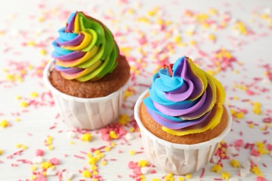 Photo of Delicious cupcakes with colorful cream and sprinkles on white wooden table, closeup