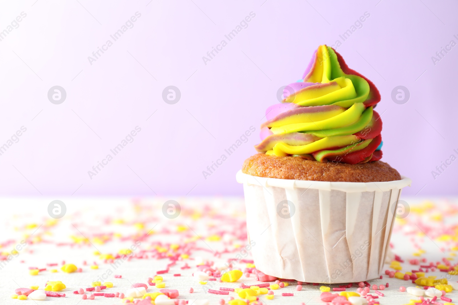 Photo of One delicious cupcake with colorful cream and sprinkles on white wooden table against violet background, closeup. Space for text