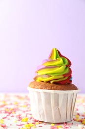 Photo of One delicious cupcake with colorful cream and sprinkles on white wooden table against violet background, closeup. Space for text