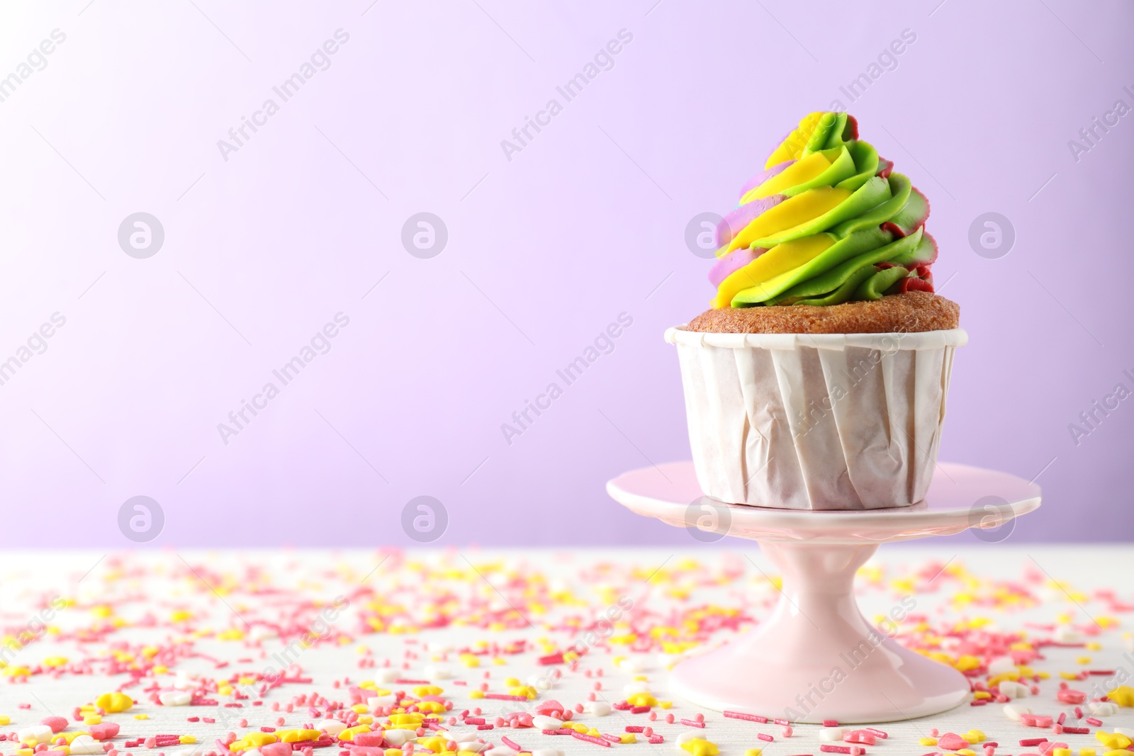 Photo of One delicious cupcake with colorful cream and sprinkles on white wooden table against violet background, closeup. Space for text