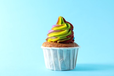 Photo of One delicious cupcake with colorful cream on light blue background, closeup