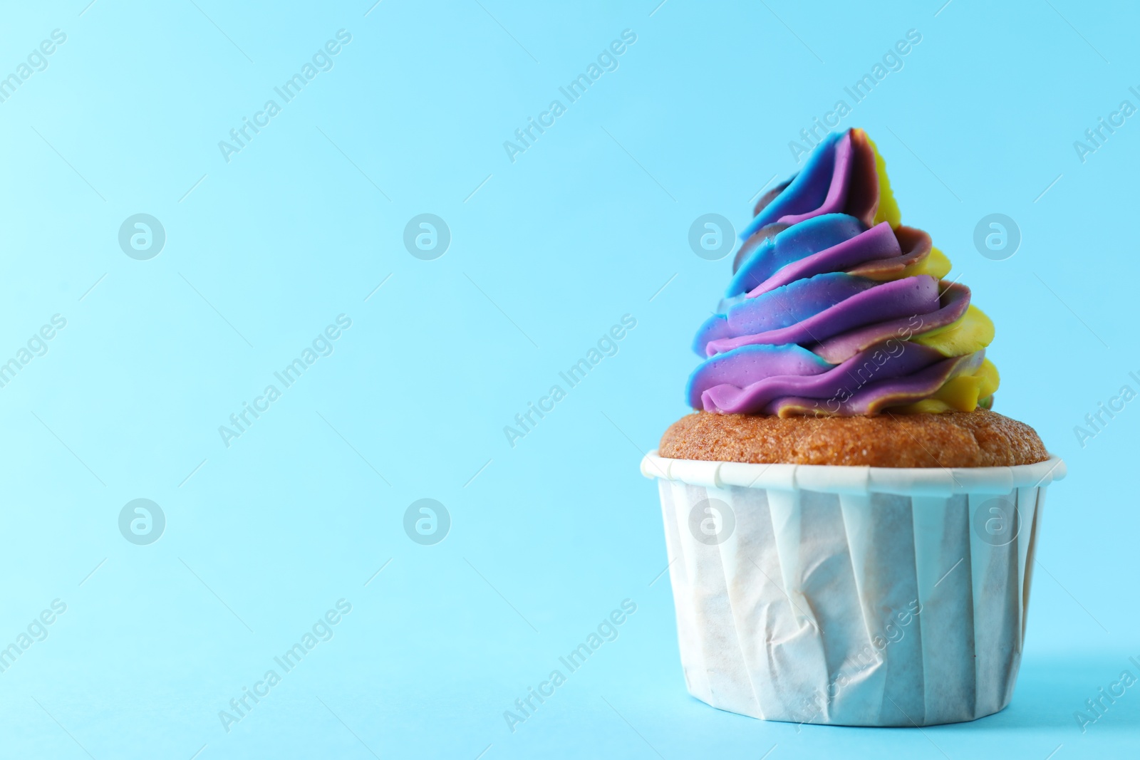 Photo of One delicious cupcake with colorful cream on light blue background, closeup. Space for text