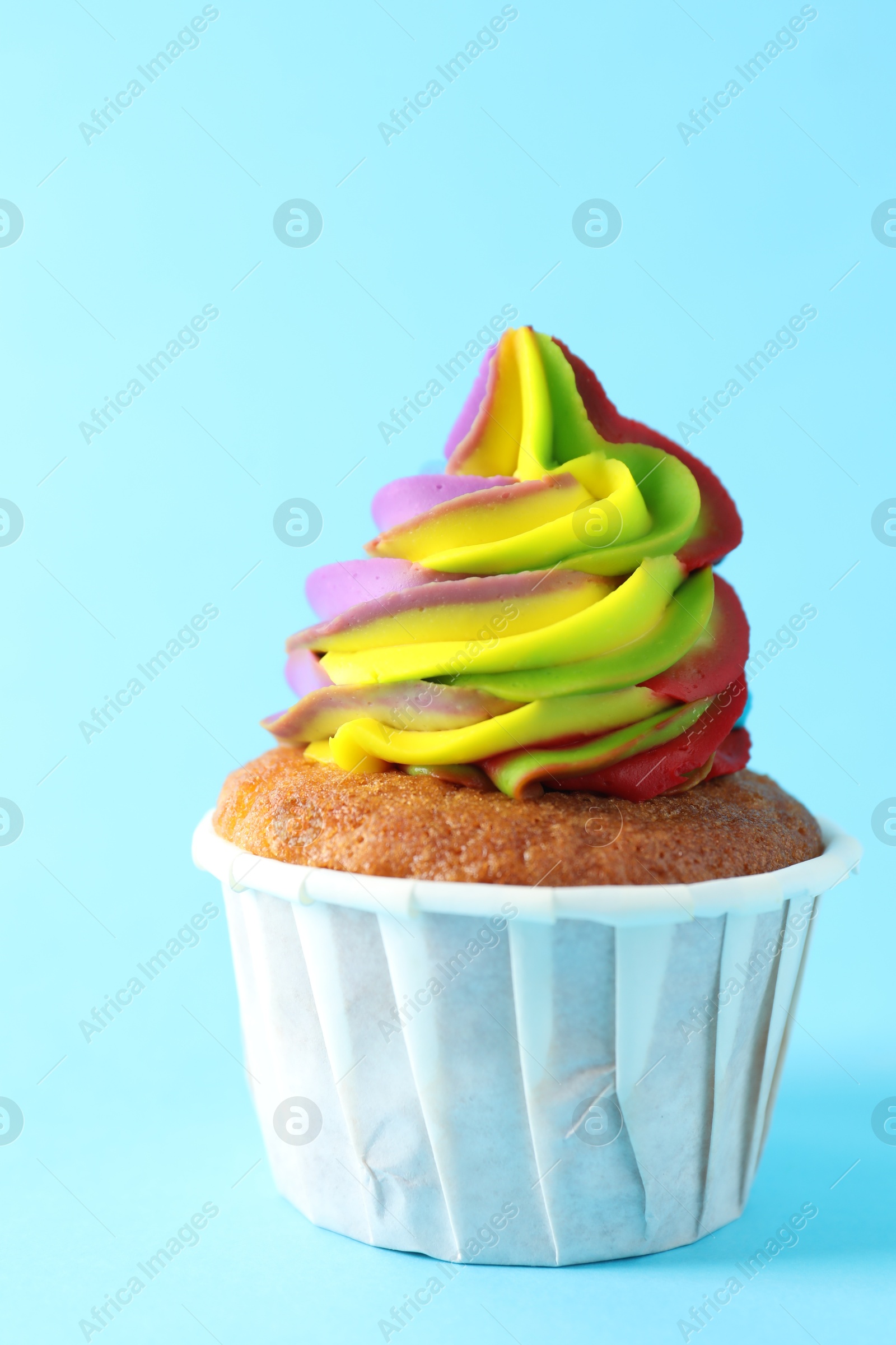 Photo of One delicious cupcake with colorful cream on light blue background, closeup