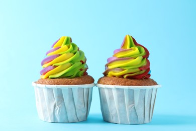 Photo of Delicious cupcakes with colorful cream on light blue background, closeup