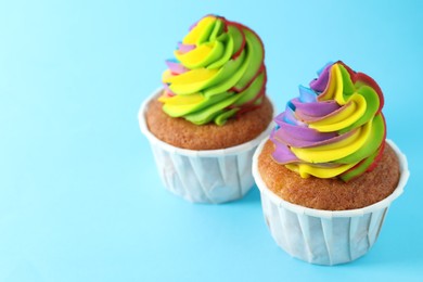 Photo of Delicious cupcakes with colorful cream on light blue background, closeup. Space for text