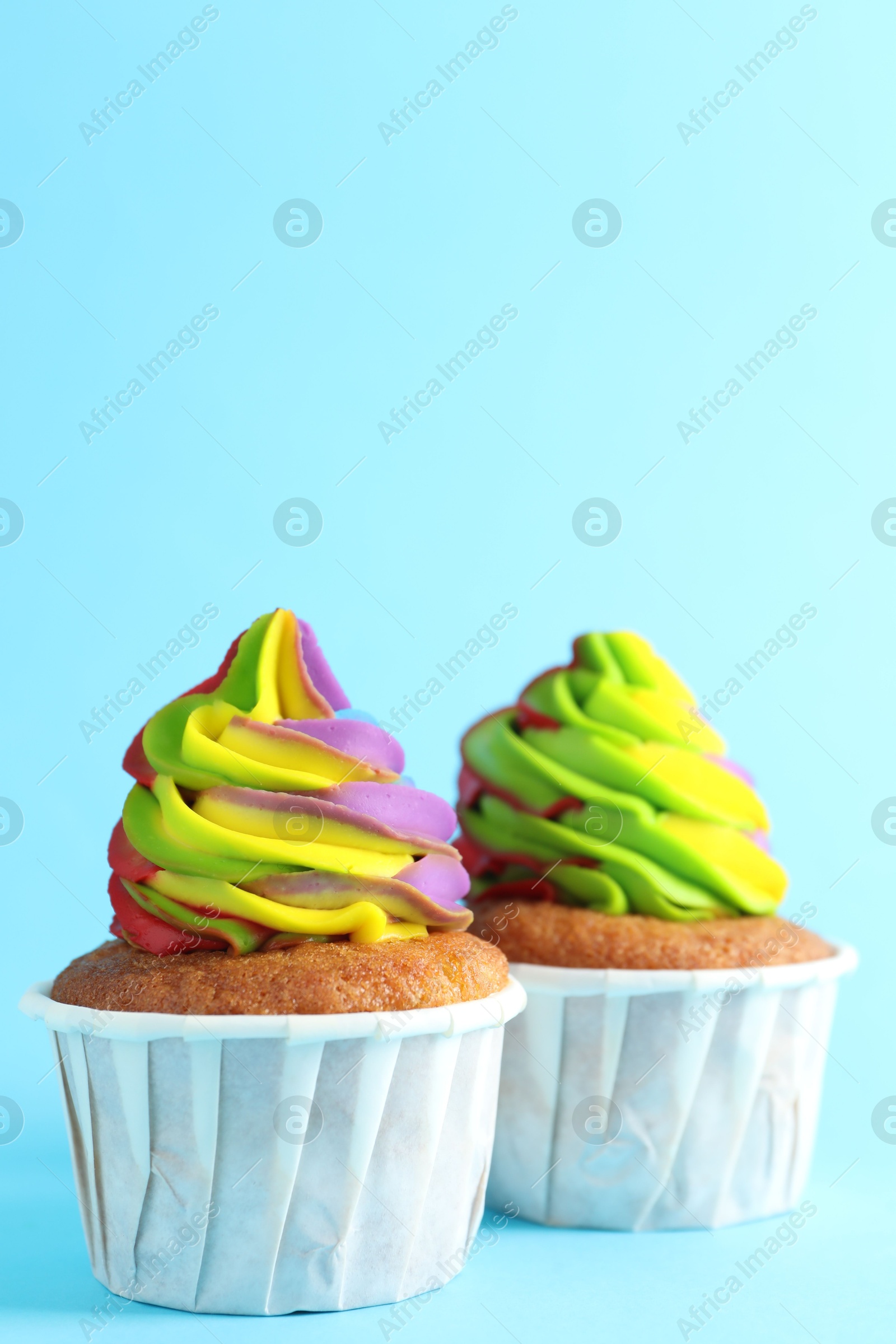 Photo of Delicious cupcakes with colorful cream on light blue background, closeup