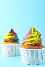 Photo of Delicious cupcakes with colorful cream on light blue background, closeup