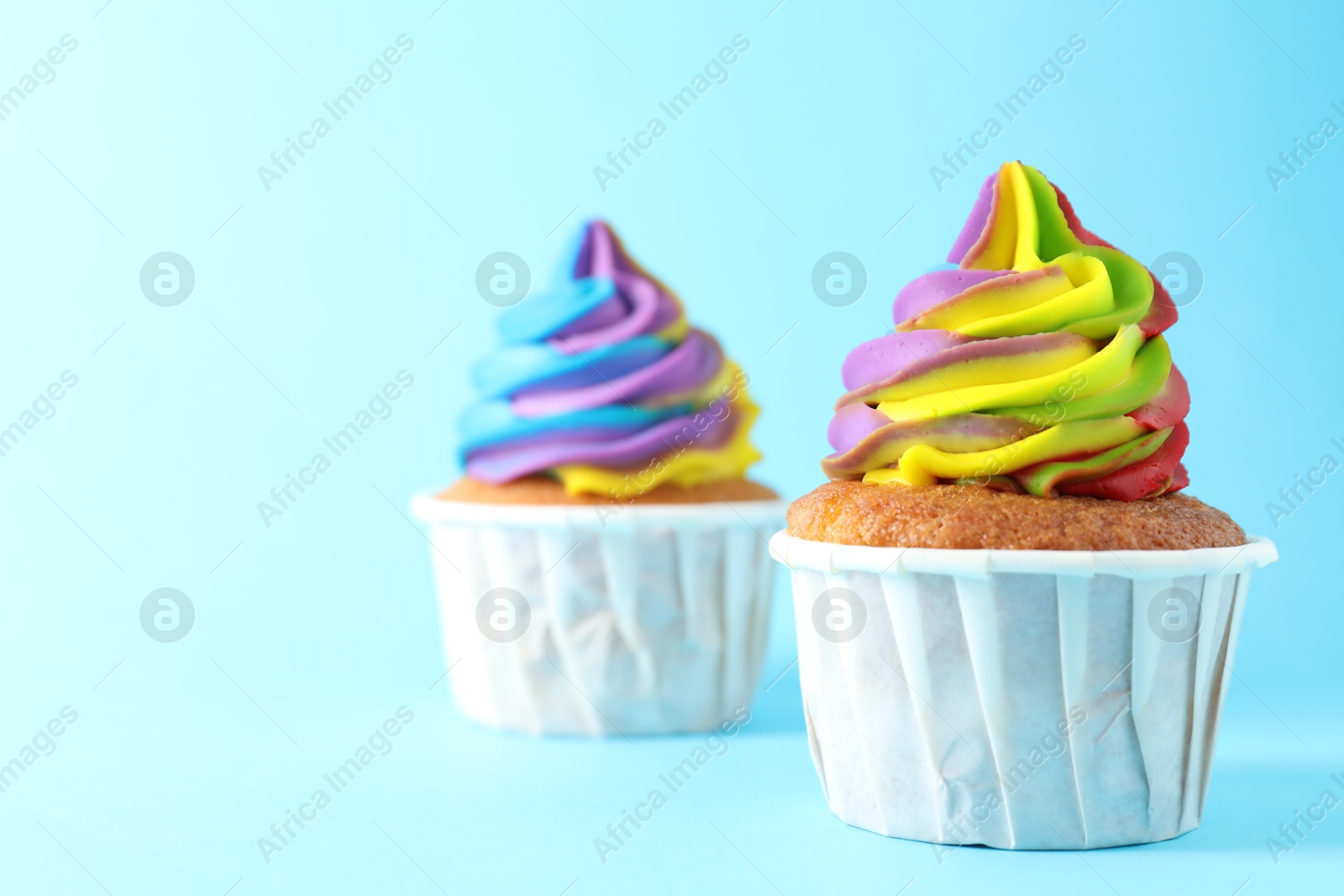 Photo of Delicious cupcakes with colorful cream on light blue background, closeup. Space for text