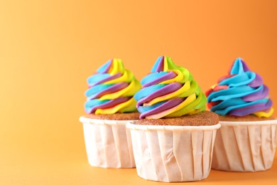 Photo of Delicious cupcakes with colorful cream on orange background, closeup. Space for text