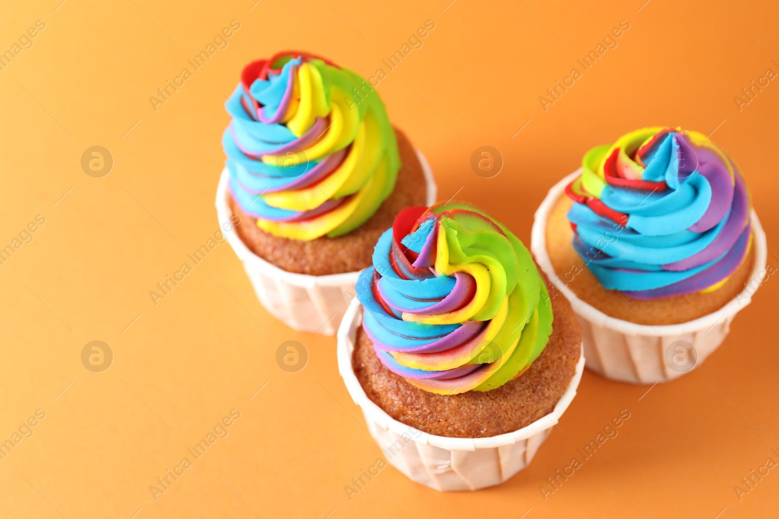 Photo of Delicious cupcakes with colorful cream on orange background, closeup. Space for text