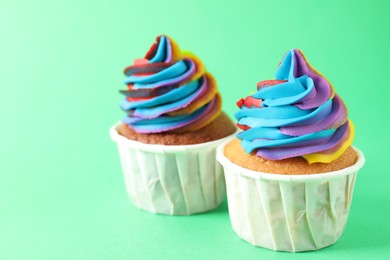 Photo of Delicious cupcakes with colorful cream on green background, closeup