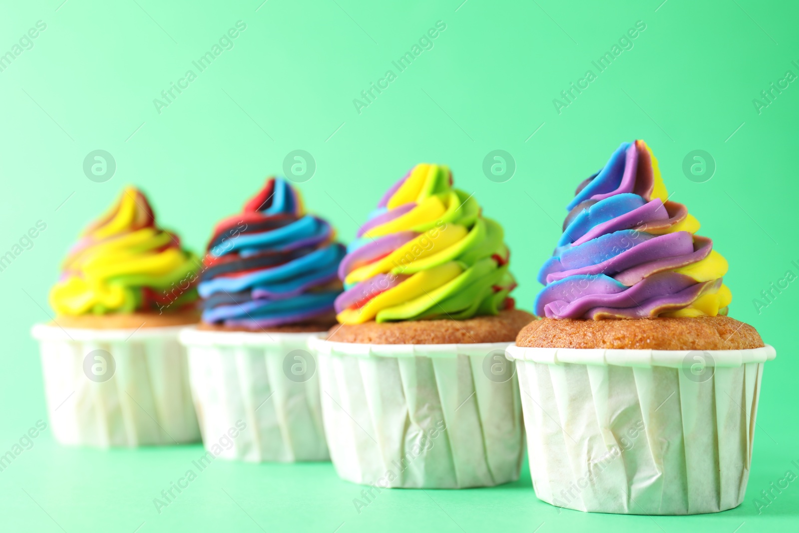 Photo of Delicious cupcakes with colorful cream on green background, closeup