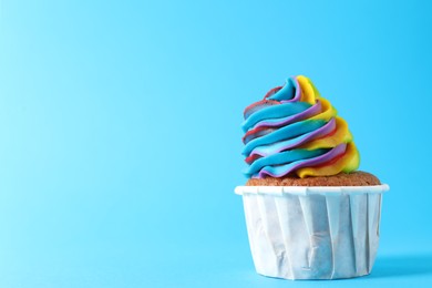 Photo of One delicious cupcake with colorful cream on light blue background, closeup. Space for text