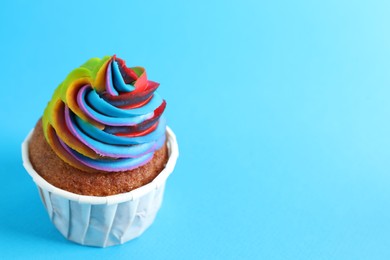 Photo of One delicious cupcake with colorful cream on light blue background, closeup. Space for text