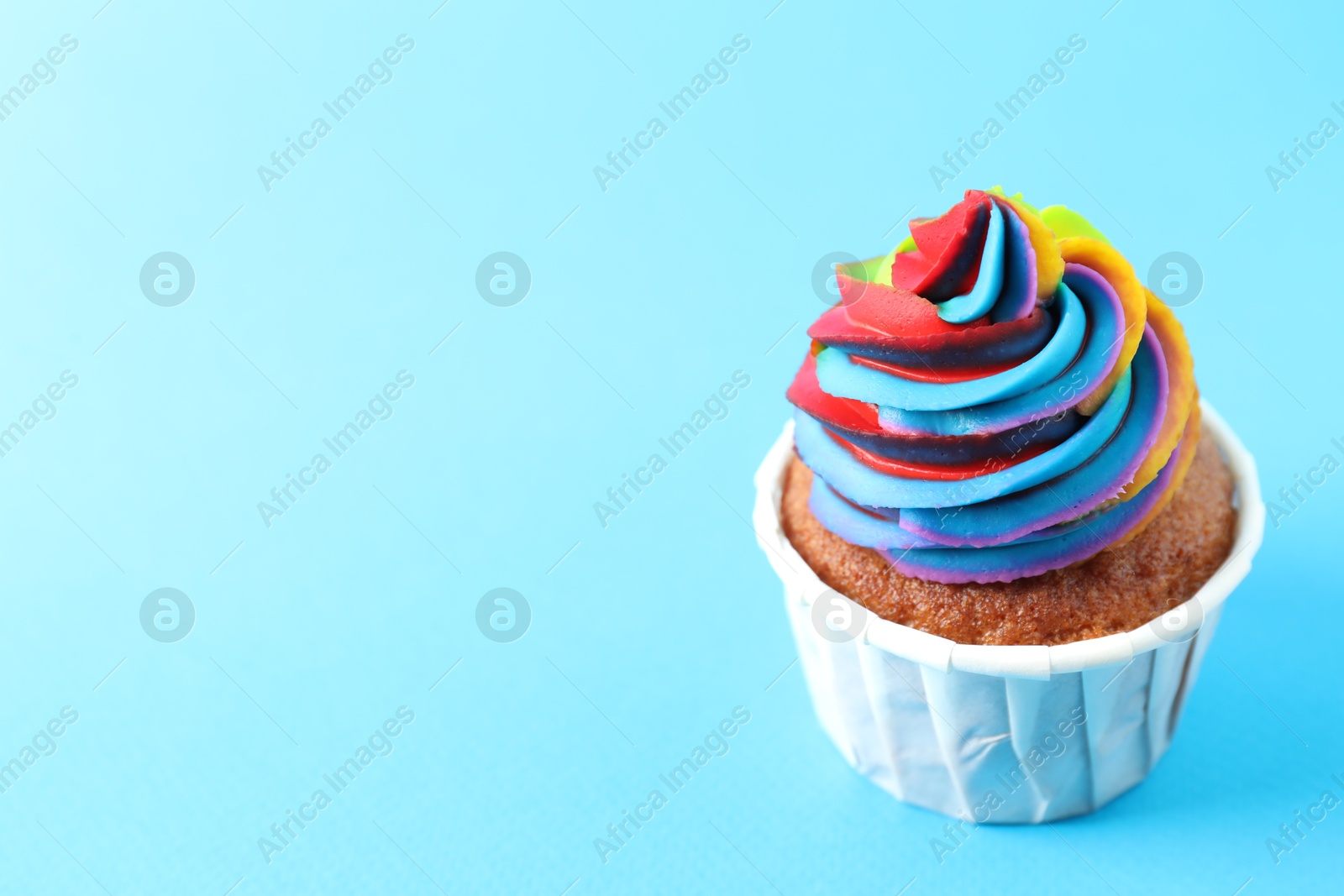 Photo of One delicious cupcake with colorful cream on light blue background, closeup. Space for text